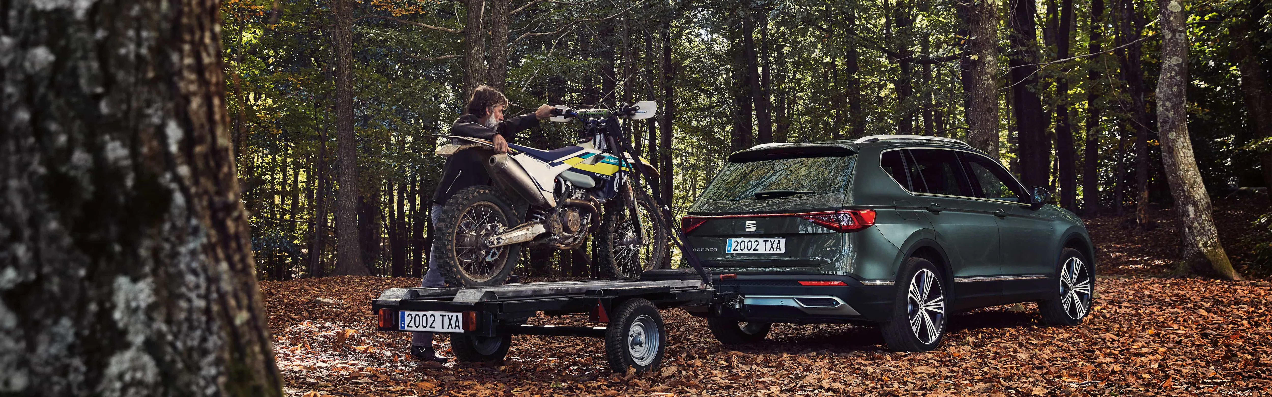 Mężczyza zdejmujący motocykl z przyczepki podłączonej do SEAT-a Tarraco w kolorze Dark Camouflage w lesie